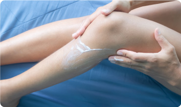 Woman applying waxy balm to her leg whilst sat on a blue sheet