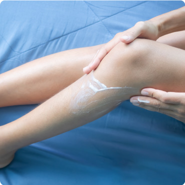 Woman applying waxy balm to her leg whilst sat on a blue sheet