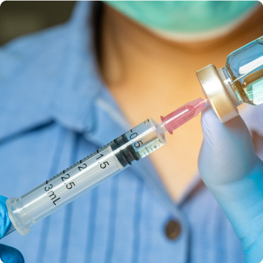 doctor's hand holds a syringe and a blue vaccine bottle at the hospital.