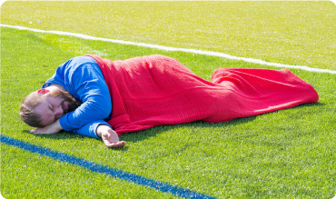 Man with cellular ambulance blanket over him lying down on a sports pitch