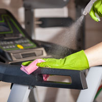 Someone spraying and wiping down gym equipment