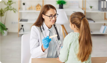 Doctor examining a young girl with a tongue depressor in their hand