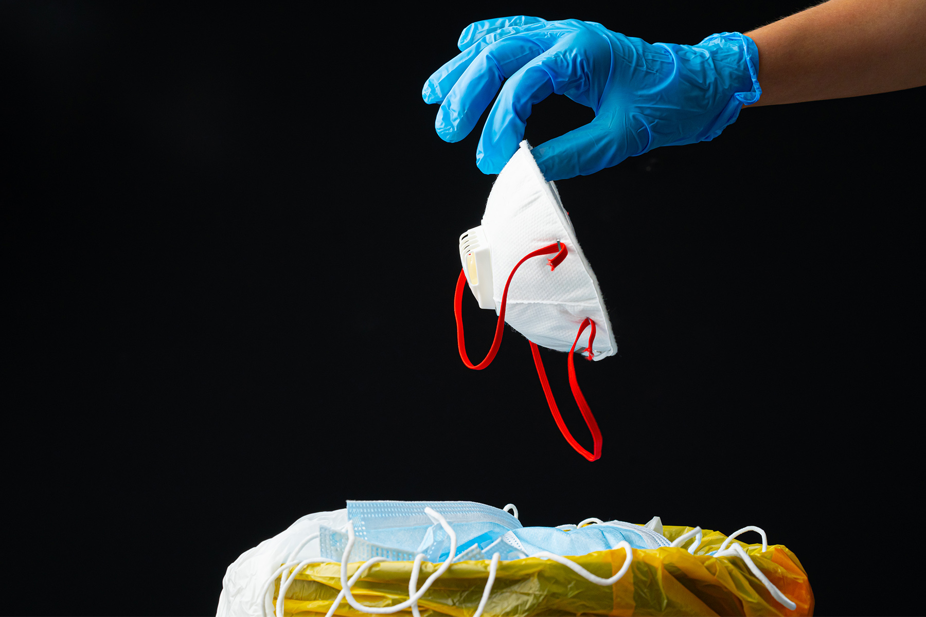 Hand putting used dirty surgical mask to a garbage bin