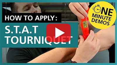 Video thumbnail showing a close-up of a person applying a red S.T.A.T. tourniquet on their arm. Text reads 'How to Apply: S.T.A.T Tourniquet' with a yellow badge saying 'One Minute Demos'. A play button is centred on the image.