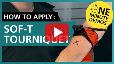 Video thumbnail showing a person applying an orange SOF-T tourniquet on an arm marked with an 'X'. Text reads 'How to Apply: SOF-T Tourniquet' with a yellow badge saying 'One Minute Demos'. A play button is centred on the image.