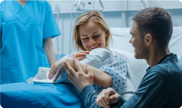 In a hospital bed the mother holds her newborn baby, supportive father next to them