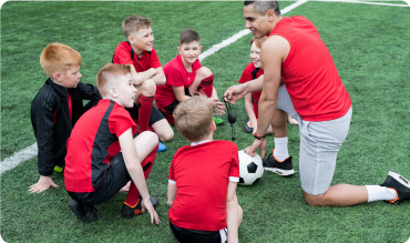PE Teacher giving pep talk to his school students on a football pitch