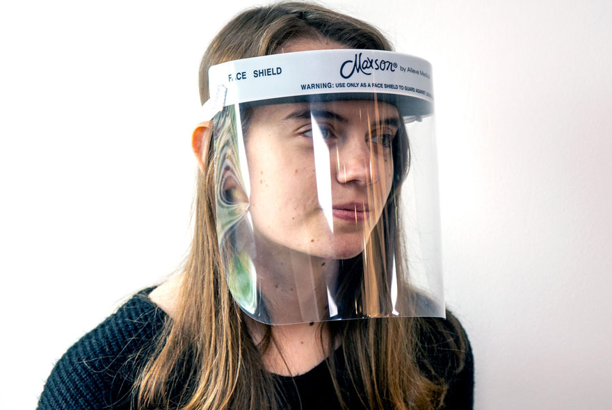 A woman wearing a Maxson-branded clear plastic face shield with a white headband, designed for personal protection against splashes and droplets, displayed against a neutral background.