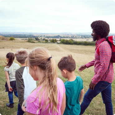 Adult Team Leader With Group Of Children At Outdoor Activity Camp Walking Through Countryside