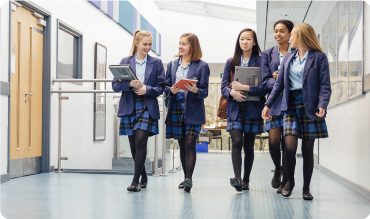 Five female school pupils walking in the school corridor together in their school uniform