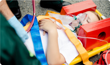Young boy on stretcher with spider straps harnessing him on the stretcher and a head immobiliser on his head