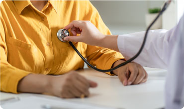 Doctor using a stethoscope to listen to a patients chest. The patient is wearing a yellow blouse