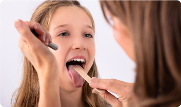 Girl getting her throat inspected by doctor using a tongue depressor and pen torch