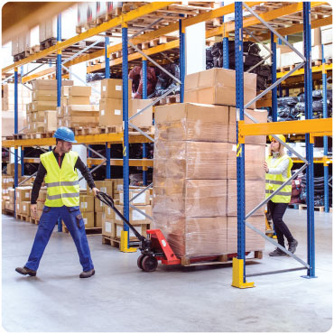 A man and a woman moving a pile of boxes in a warehouse