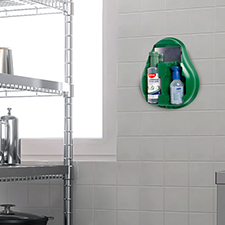 A green wall-mounted eye wash station containing two bottles of solution in a kitchen setting.