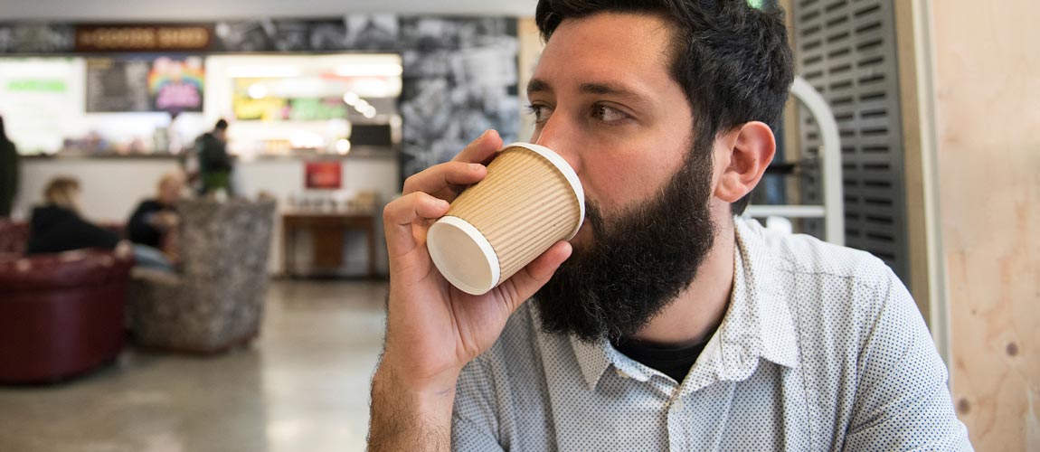 man drnking from disposal cup in cafe