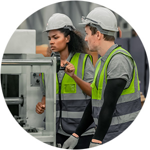 Two workers in high-visibility vests operating machinery in a manufacturing plant