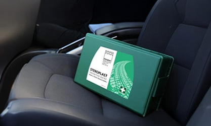 A green vehicle first aid kit labelled 'Steroplast' placed on the passenger seat of a car with a dark interior.