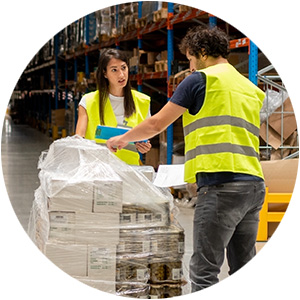 Two workers in high-visibility vests checking items in a warehouse