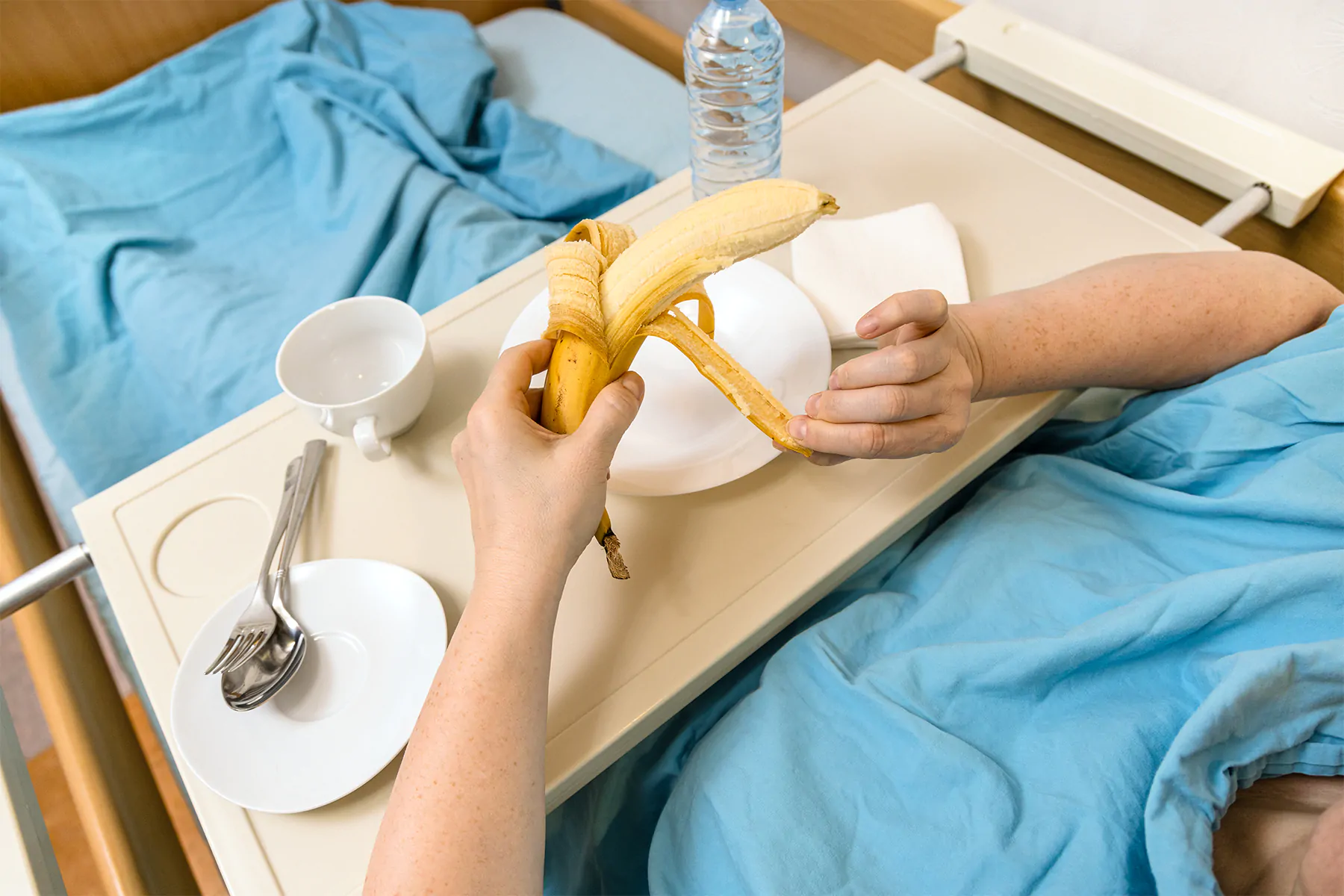 woman in homecare hospital bed with banana and metal cutlery woman in homecare hospital bed with banana and metal cutlery