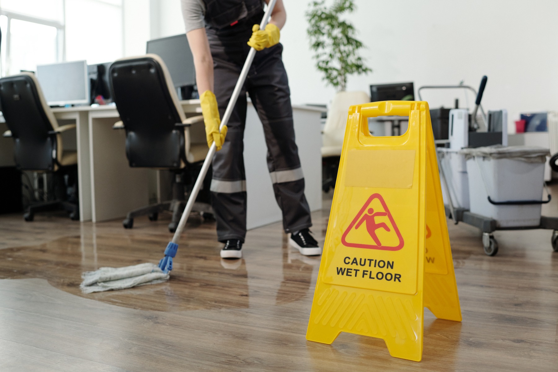 Yellow plastic signboard with caution warning about wet floor and female cleaner